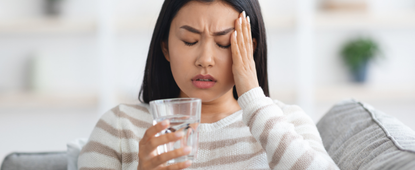 asian woman on sofa with a headache drinking glass of water