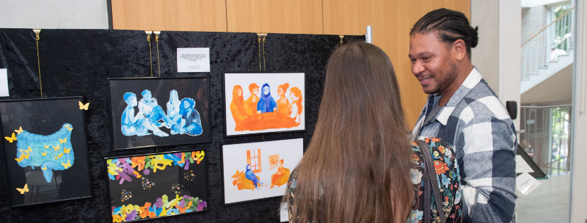 Two people talking in front of a small exhibtion of drawings relating to eating disorders