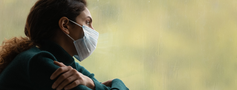 woman wearing covid-19 mask looking out of a window