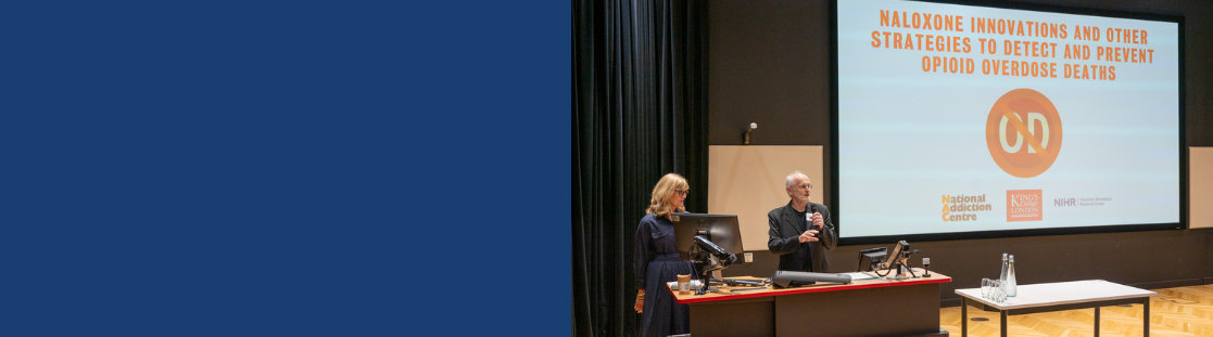 People on a stage giving a talk in a lecture theatre, the slide show behind has the name of the conference