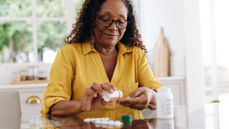 older black woman taking pills, sat at a table