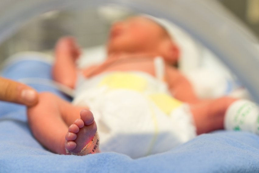 A newborn baby lies in an incubator, wrapped in a blue blanket