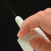 Close-up of a hand spraying a white nasal spray against a black background