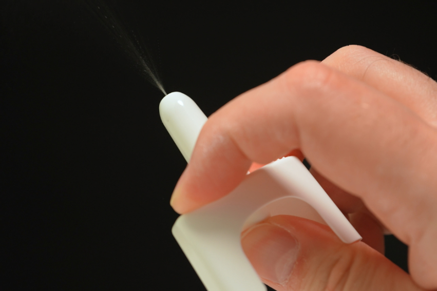 Close-up of a hand spraying a white nasal spray against a black background