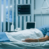 A patient lies in a hospital bed, connected to monitors