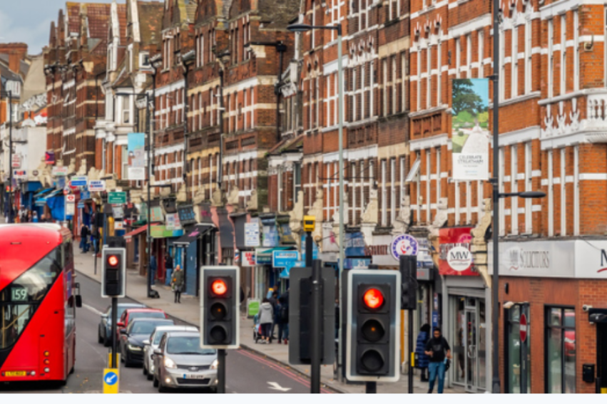 A bustling London street features a classic red double-decker bus and vibrant redbrick buildings