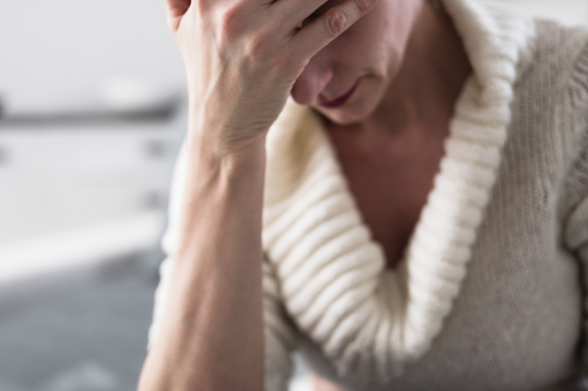 A person in a cozy sweater holds their forehead, appearing stressed or fatigued
