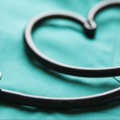 A stethoscope forms a heart shape on a teal medical scrub top