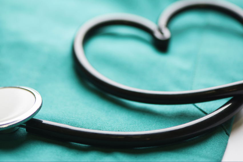A stethoscope forms a heart shape on a teal medical scrub top