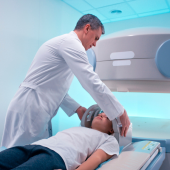 A man doctor in a white coat adjusts a child patient's head for an MRI scan in a brightly lit room