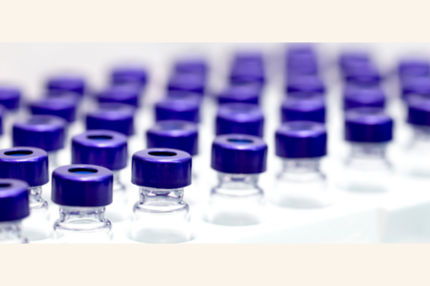 Rows of clear glass vials with purple caps are lined up in a lab setting.