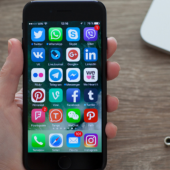 A hand holds a smartphone displaying various social media app icons on its screen