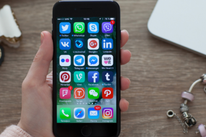 A hand holds a smartphone displaying various social media app icons on its screen