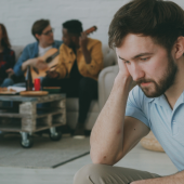 A man in the foreground appears sad and isolated at a social gathering