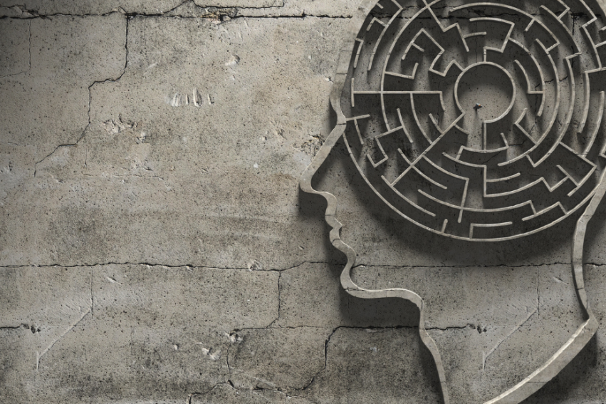 Silhouette of a human head with a maze inside against a cracked, concrete wall