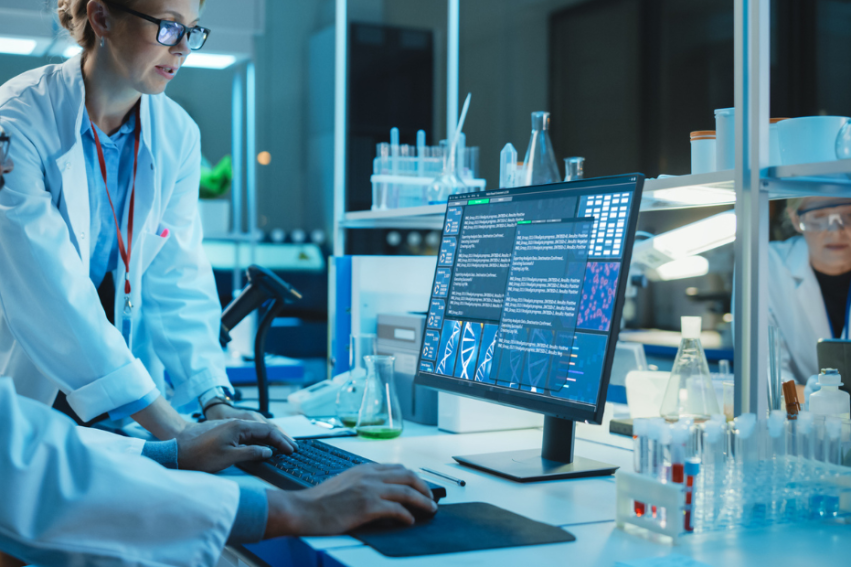 In a dimly lit lab, three scientists in white coats analyze data on a computer.