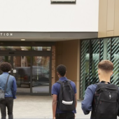 Students with backpacks walk towards a modern building's main reception entrance
