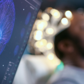A computer screen displays a vivid, glowing neural network while a person sits in the background wearing electrodes, suggesting a brain-computer interface study.