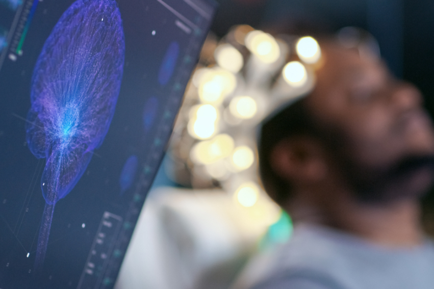 A computer screen displays a vivid, glowing neural network while a person sits in the background wearing electrodes, suggesting a brain-computer interface study.