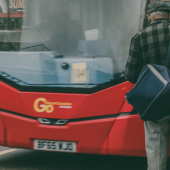 An elderly man with a blue bag boards a red city bus