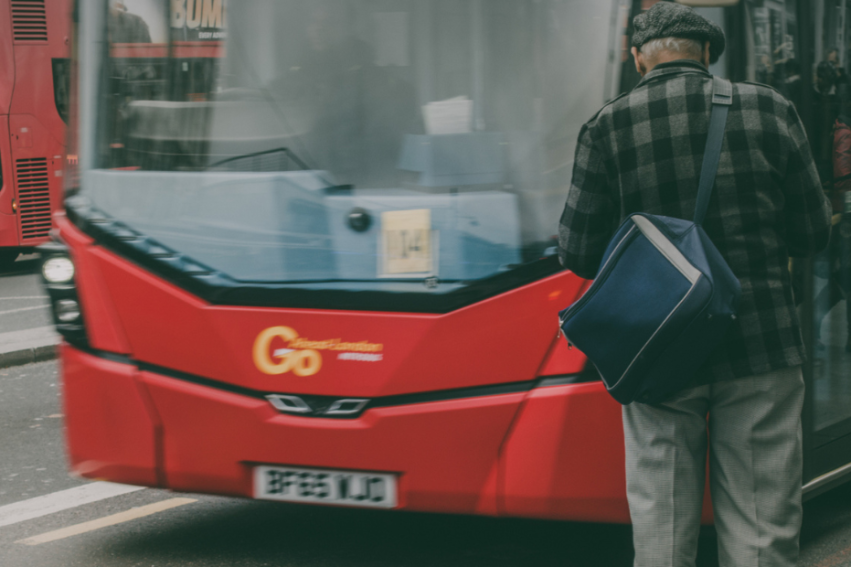 An elderly man with a blue bag boards a red city bus