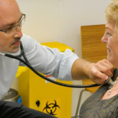 A male doctor listens to an elderly woman's heartbeat with a stethoscope in a clinic