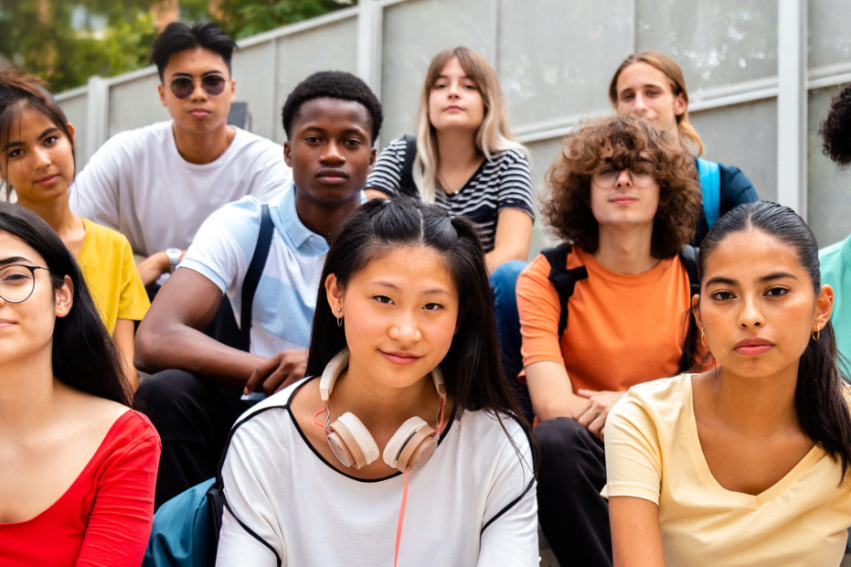 A diverse group of ten serious-looking teens sits on outdoor steps