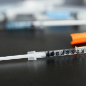 A syringe with an orange cap lies on a dark surface
