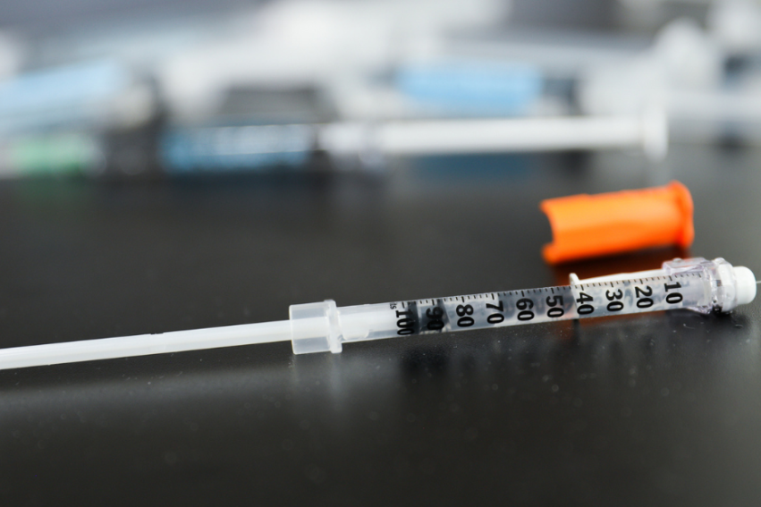 A syringe with an orange cap lies on a dark surface