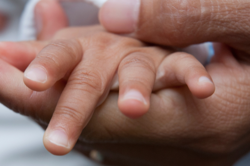 A close-up of an adult hand gently holding a baby's tiny hand