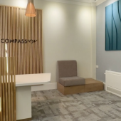 Modern waiting room with soft lighting and neutral tones. Features a wooden slat accent wall, minimalist seating, and abstract blue wall art