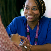 Smiling woman in blue scrubs and lanyard talks to another person