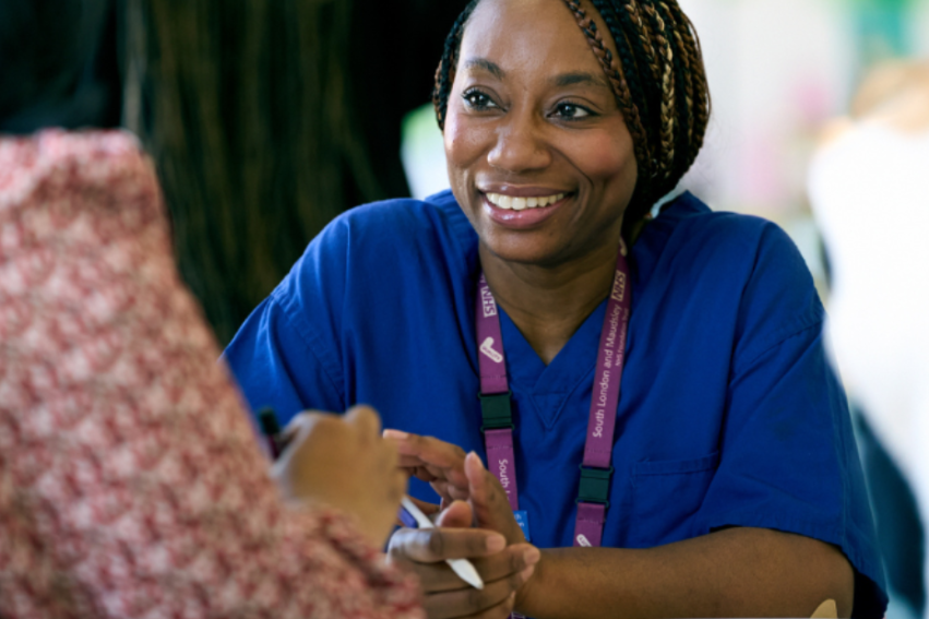 Smiling woman in blue scrubs and lanyard talks to another person