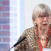 A woman with glasses speaks into a microphone at a lectern