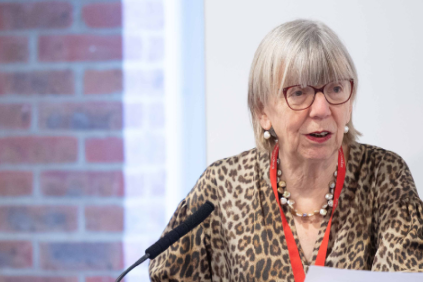 A woman with glasses speaks into a microphone at a lectern