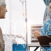 A female nurse in scrubs smiles while discussing with an older woman in a hospital setting