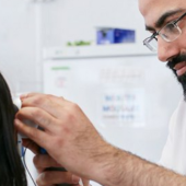 A healthcare professional with glasses and a beard examines a patient's ear in a clinical setting
