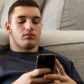 Young man lying on a gray couch scrolling on his smartphone