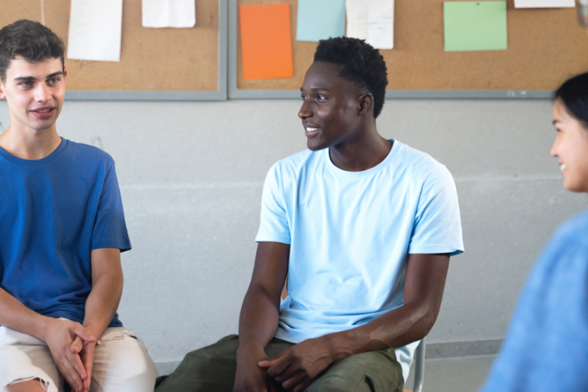 A diverse group of young adults sits in a circle, engaging in a lively discussion