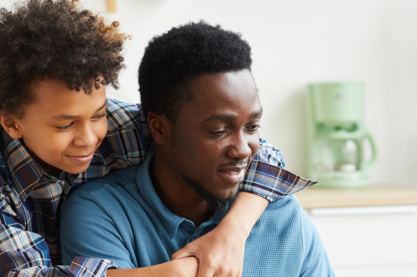 Father and son smiling, with the son playfully hugging the father from behind