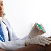 A healthcare professional in a white coat administers a vaccine to an older man.