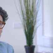 A woman with short curly hair and glasses sits in an office
