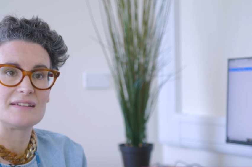 A woman with short curly hair and glasses sits in an office