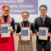 Five people stand smiling, holding certificates in an office setting