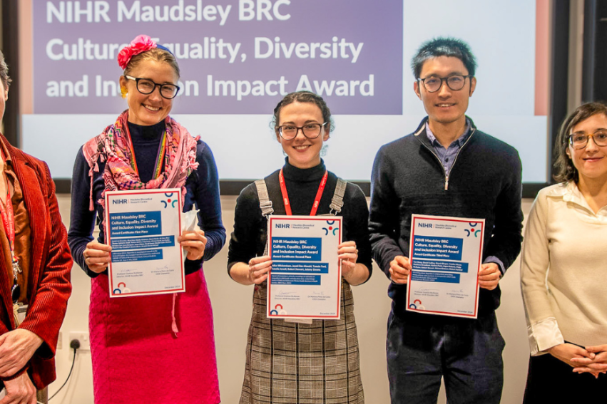 Five people stand smiling, holding certificates in an office setting
