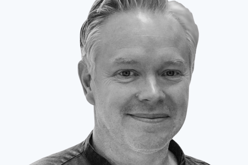 A man with short, light hair smiles warmly in a black-and-white portrait