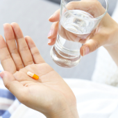 A person is holding a pill and a glass of water, preparing to take medication