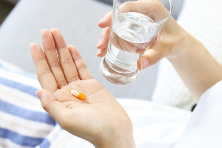 A person is holding a pill and a glass of water, preparing to take medication