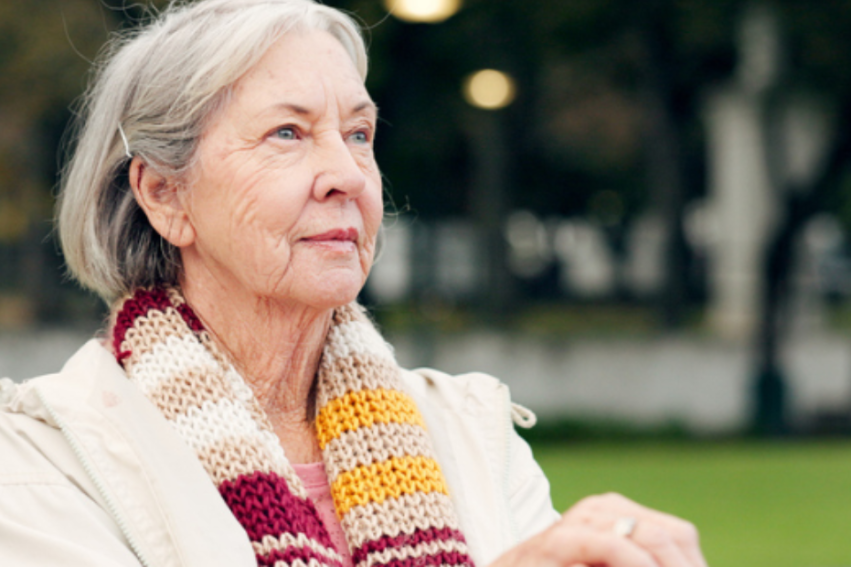 An older woman sat on a bench in a park