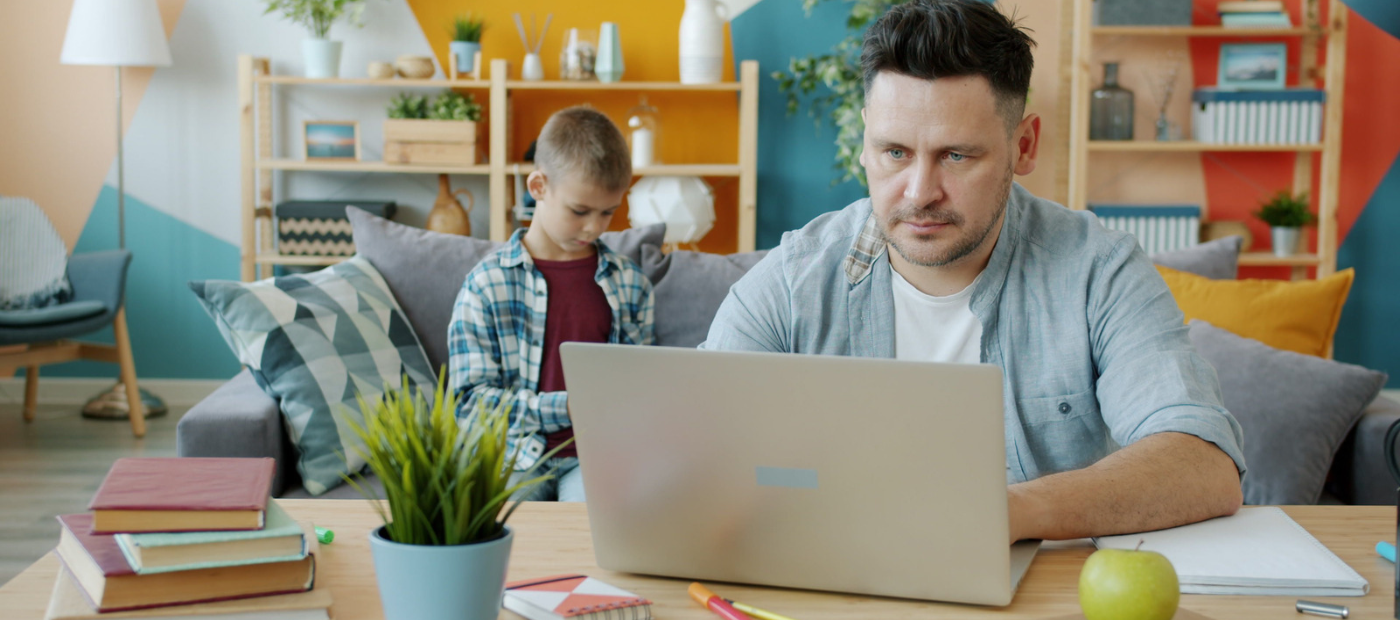 father on laptop and son in background
